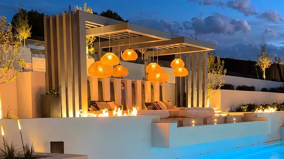 Steel pergola with vertical fin screen lit at dusk beside a swimming pool
