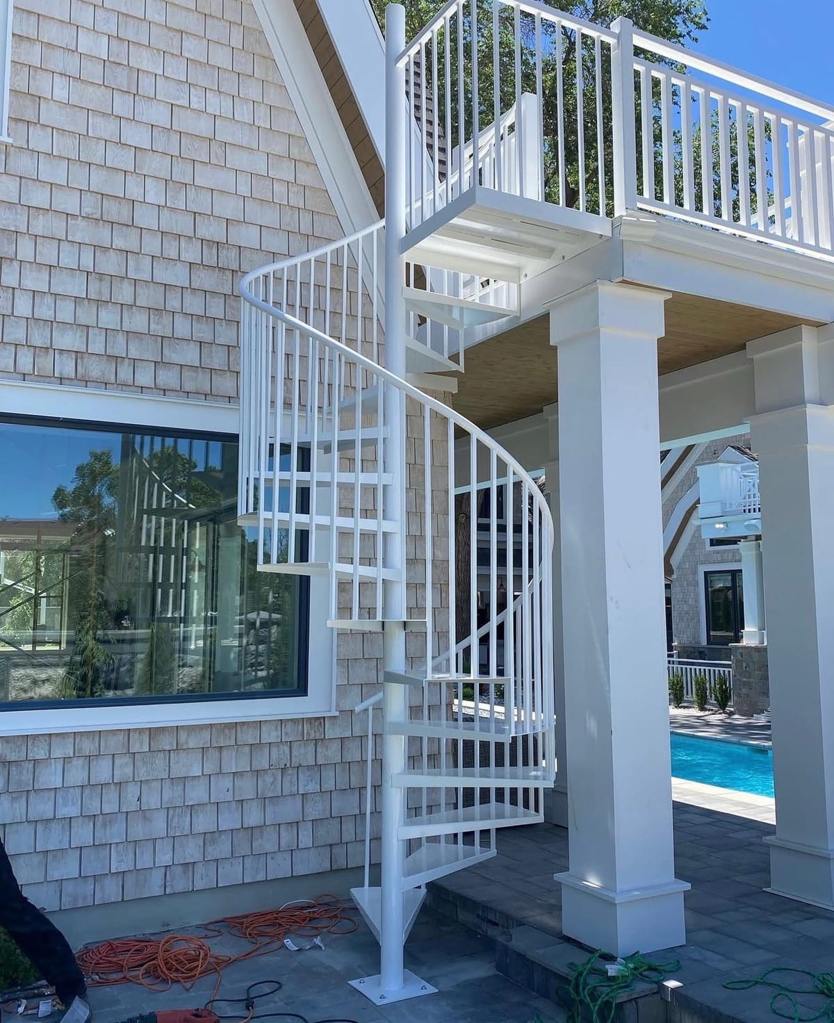 White powder-coated spiral staircase connecting a shingled home's upper deck to a poolside patio
